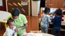 Children and a staffer in a daycare center. The children are gathered around desks and play areas.