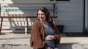 A pregnant woman sits in front of a building with her hand on her stomach.