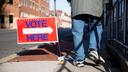 A sign with an arrow pointing right and the words "Vote Here" above it.